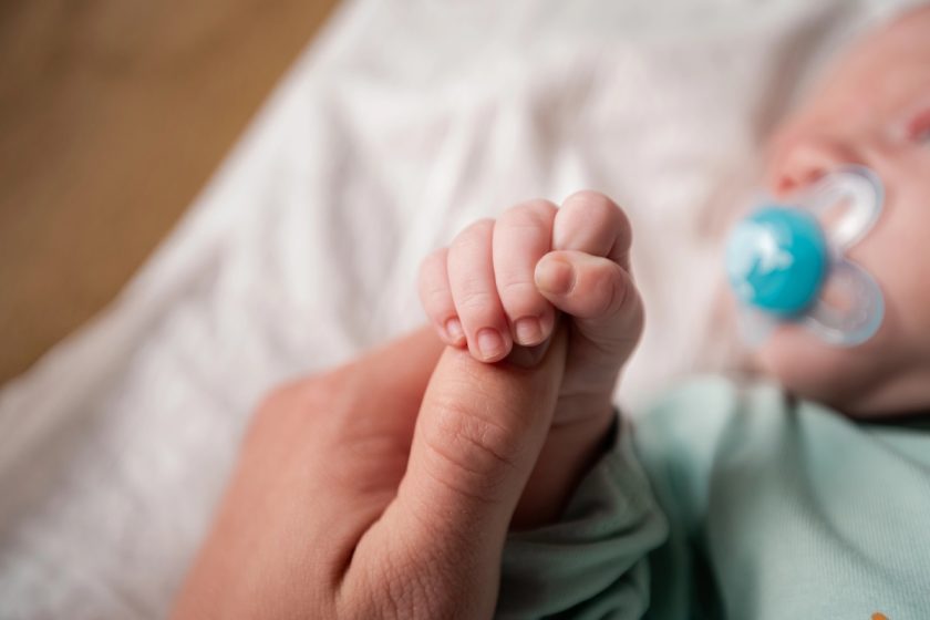 l’immagine rappresenta un neonato che che sta succhiando il ciuccio mentre tiene la mano della mamma