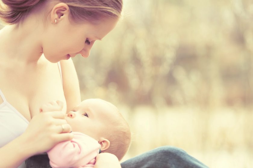 Mamma allatta il neonato in casa, immagine a tema capezzolo gonfio e cura del seno in allattamento.