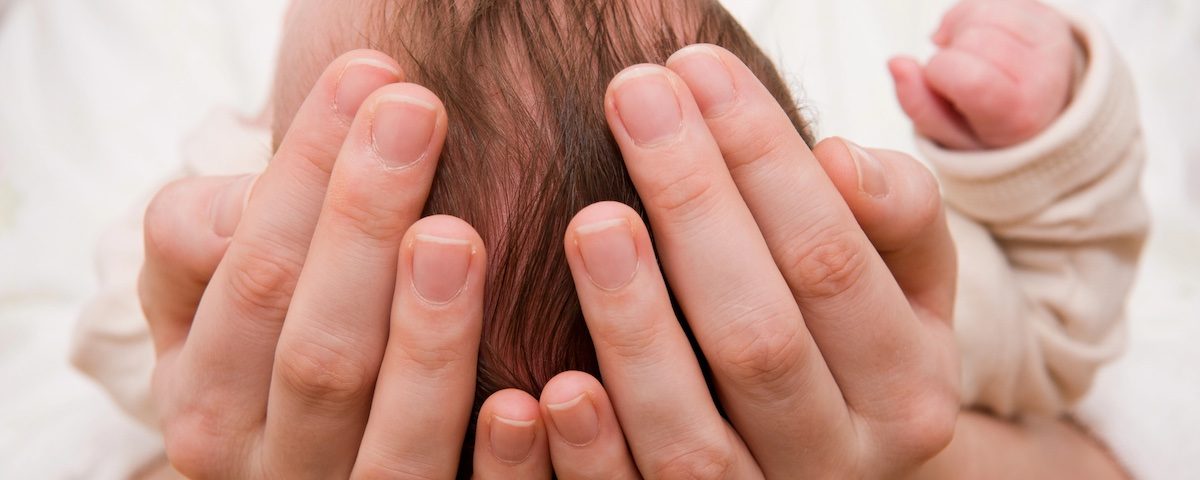 Genitore accarezza delicatamente la testolina di un neonato, immagine a tema fontanella che pulsa.
