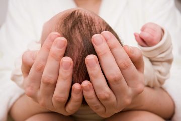 Genitore accarezza delicatamente la testolina di un neonato, immagine a tema fontanella che pulsa.