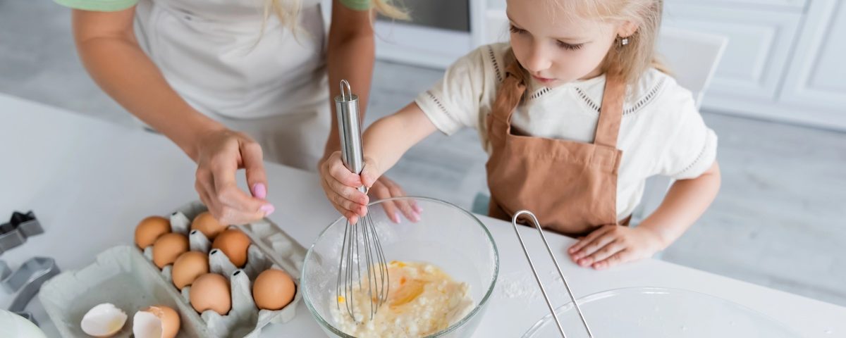 Genitore prepara una ricetta con uova in una cucina pulita, simbolo di sicurezza alimentare per bambini.