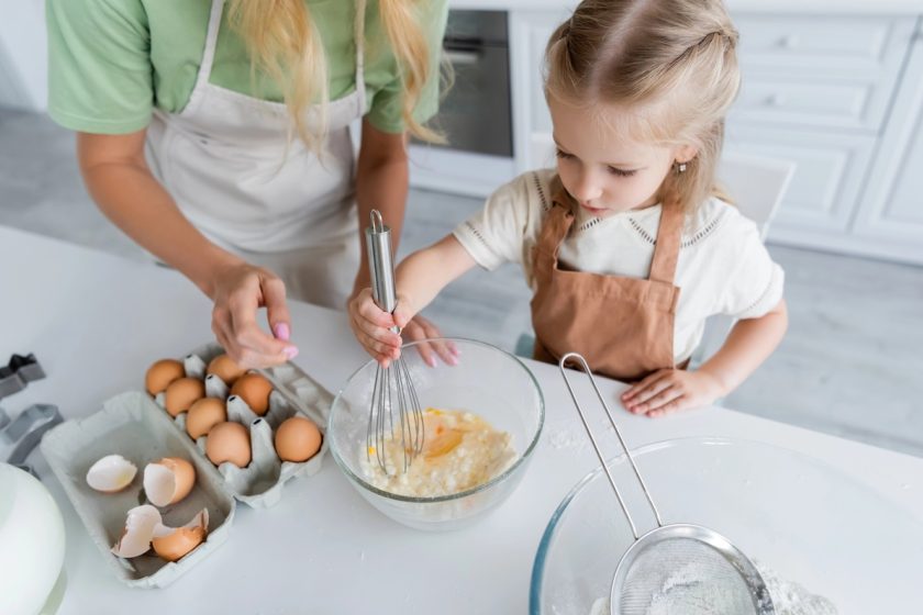 Genitore prepara una ricetta con uova in una cucina pulita, simbolo di sicurezza alimentare per bambini.